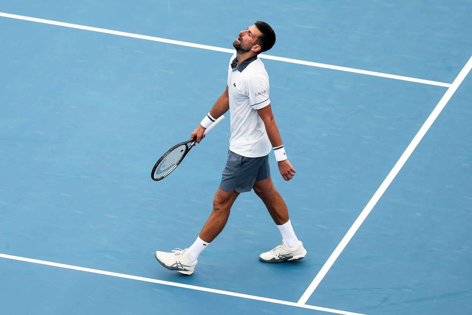 Novak Djokovic walks on the tennis court holding his racket while tilting his head back (Emilee Chinn / Getty Images)